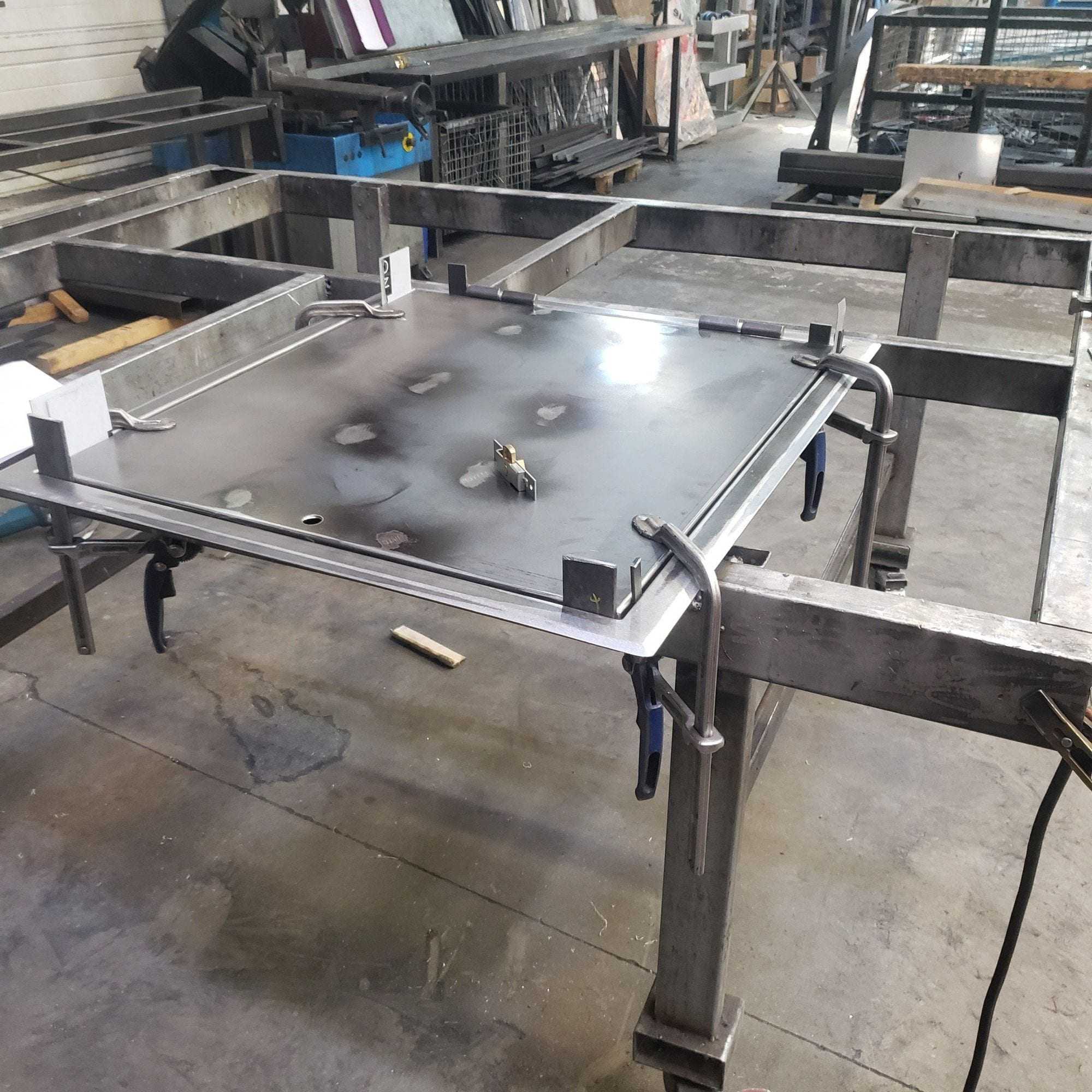 Tôle d’acier maintenue par des serre-joints sur un châssis soudé, en atelier